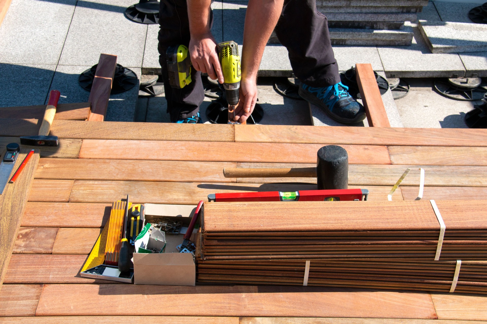 Wood deck installation worker, deck builder at work on hardwood decking terrace