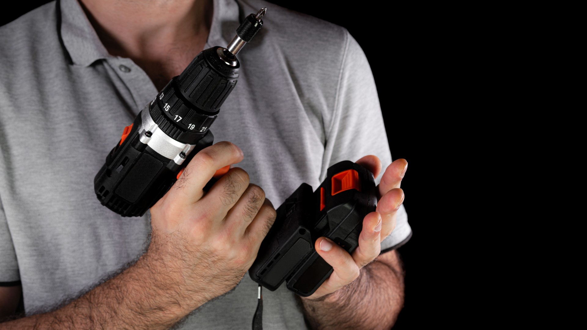 Man using a cordless drill while holding battery pack in a dark setting