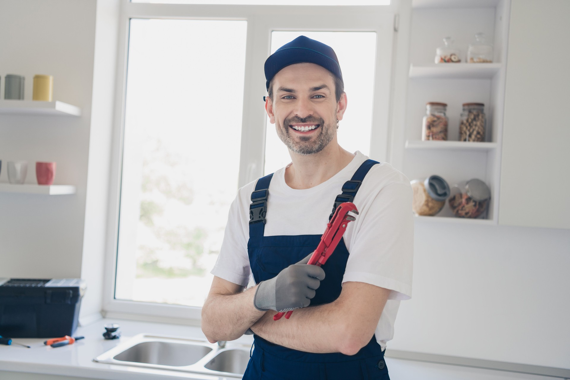 Smiling handyman in overalls holding wrench in bright modern kitchen ready for home renovation or plumbing repair